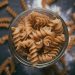 Whole wheat spiral pasta in a glass jar on a wooden table.