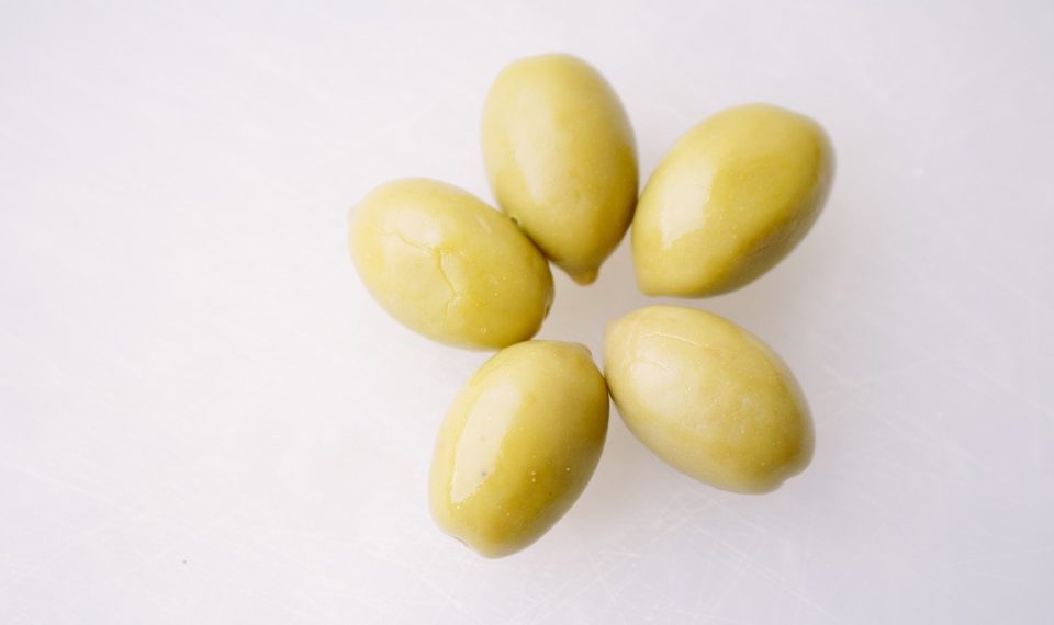 Green olives arranged on a white surface