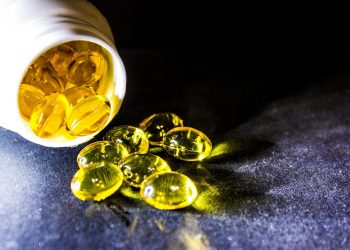Yellow capsules spilling from a bottle on black surface.