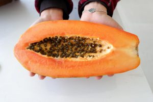 Hands holding a ripe papaya with seeds inside.