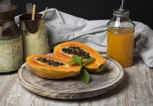 Fresh papaya halves and juice on wooden tray with mint garnish.