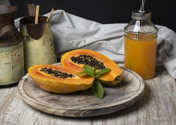 Fresh papaya halves and juice on wooden tray with mint garnish.