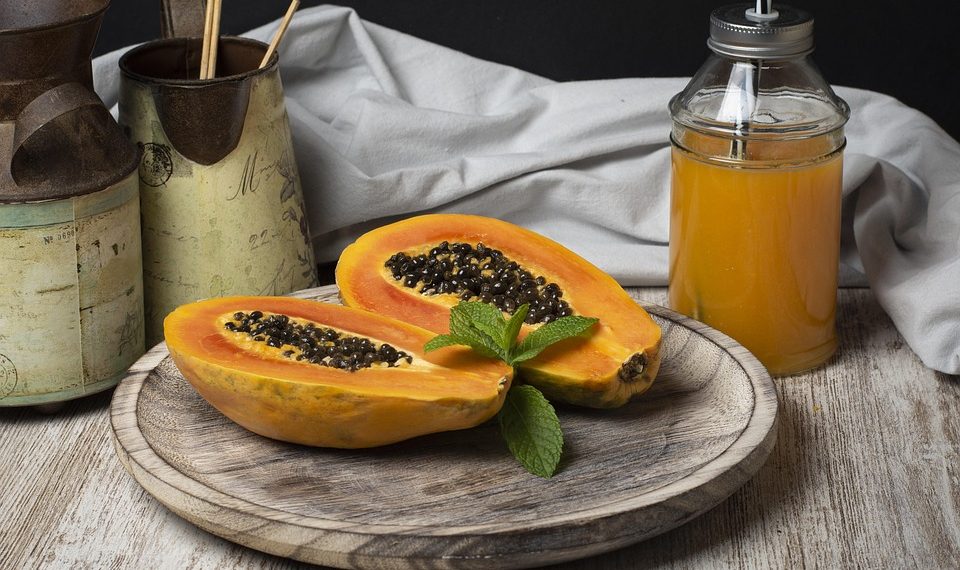 Fresh papaya halves and juice on wooden tray with mint garnish.