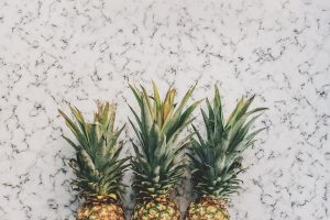 Three pineapples lined up on a marble surface.