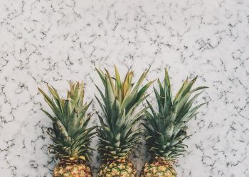 Three pineapples lined up on a marble surface.