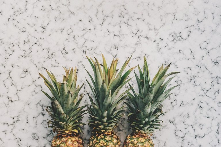 Three pineapples lined up on a marble surface.