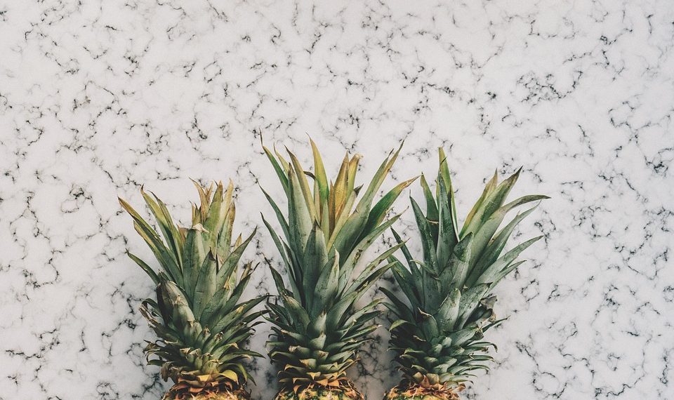 Three pineapples lined up on a marble surface.