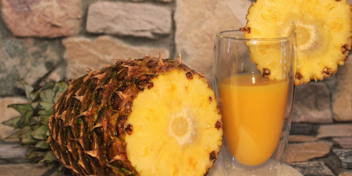 Pineapple juice in glass with fresh pineapple slice.