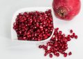 Pomegranate seeds in a bowl with whole fruit beside.