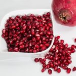 Pomegranate seeds in a bowl with whole fruit beside.