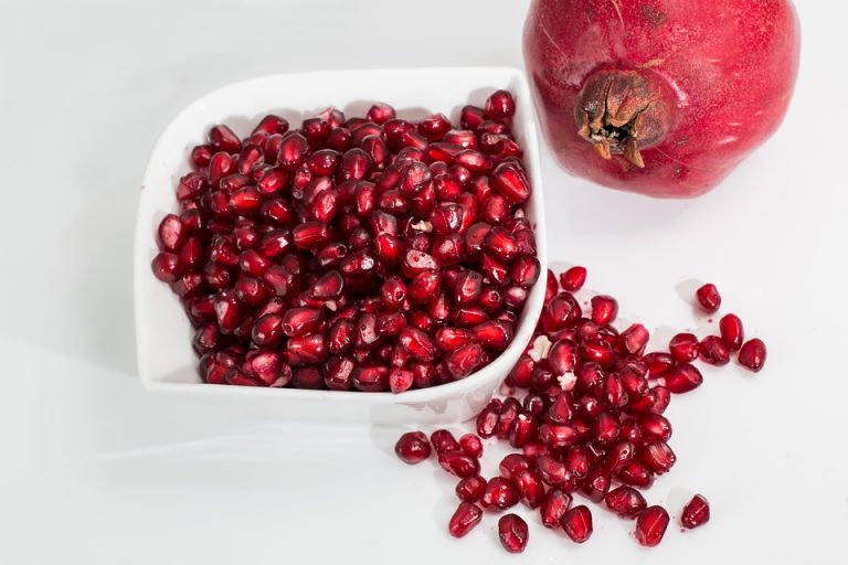 Pomegranate seeds in a bowl with whole fruit beside.