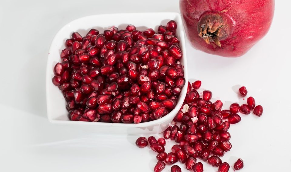 Pomegranate seeds in a bowl with whole fruit beside.