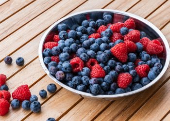 Bowl of fresh blueberries and raspberries on a wooden table.