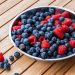 Bowl of fresh blueberries and raspberries on a wooden table.