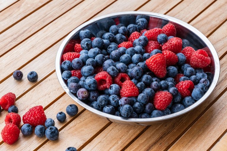 Bowl of fresh blueberries and raspberries on a wooden table.
