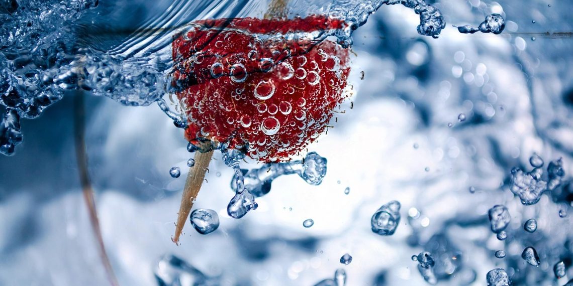 Strawberry with bubbles submerged in water.