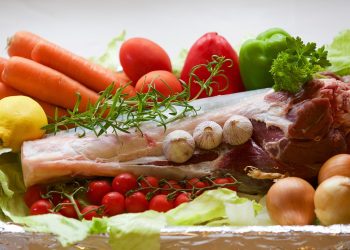 Roast lamb surrounded by fresh vegetables and herbs.