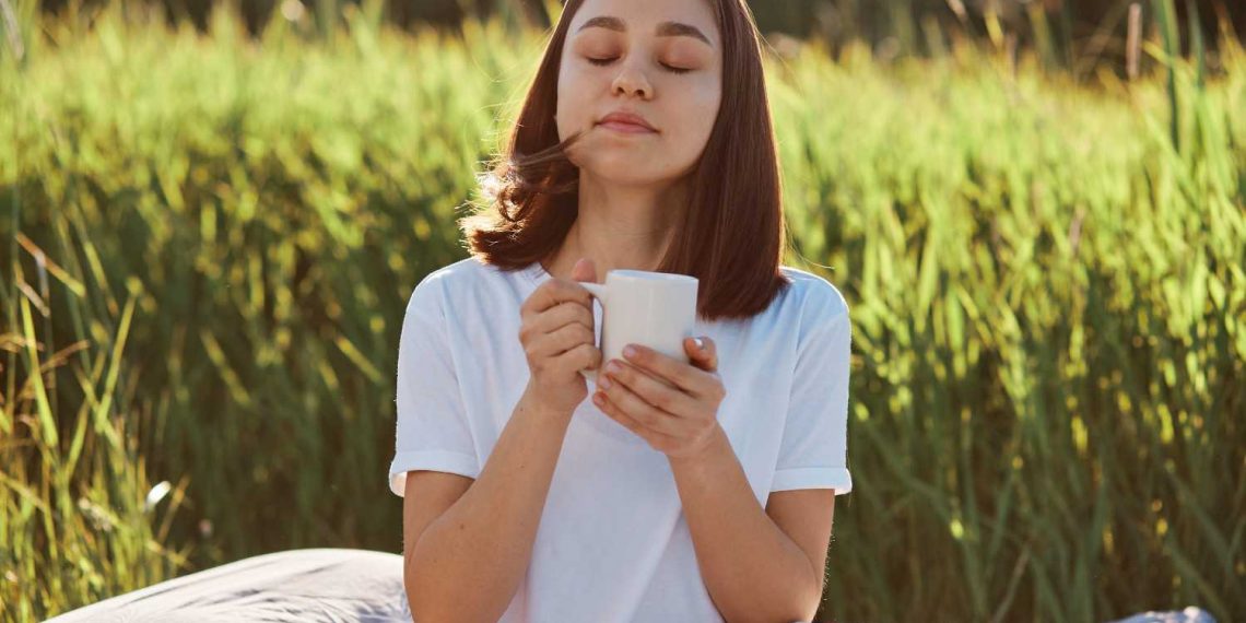 Woman enjoying a warm drink outdoors in nature.