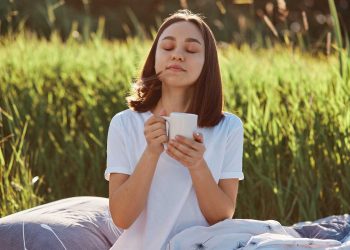 Woman enjoying a warm drink outdoors in nature.