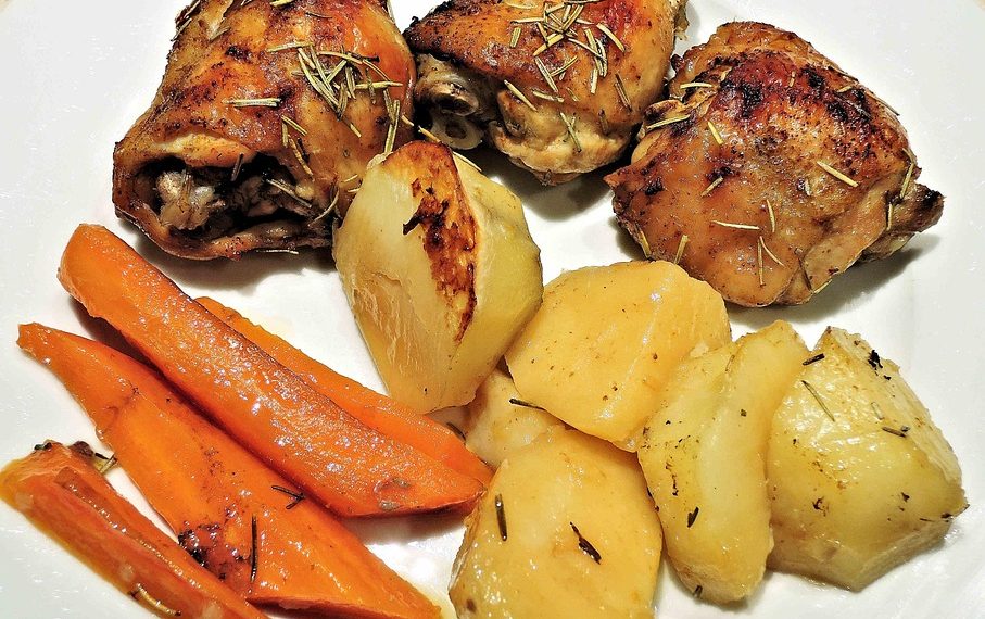 Roasted chicken with rosemary, potatoes, and carrots on a plate.