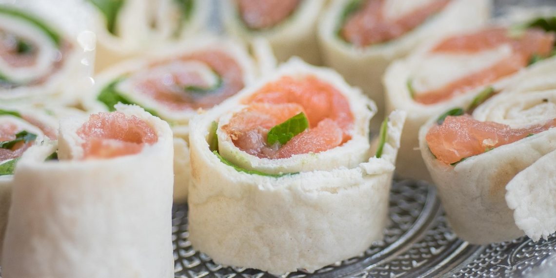 Salmon tortilla rolls with fresh greens on a plate.