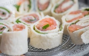 Salmon tortilla rolls with fresh greens on a plate.