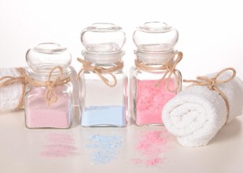 Jars of colorful bath salts with a rolled white towel.