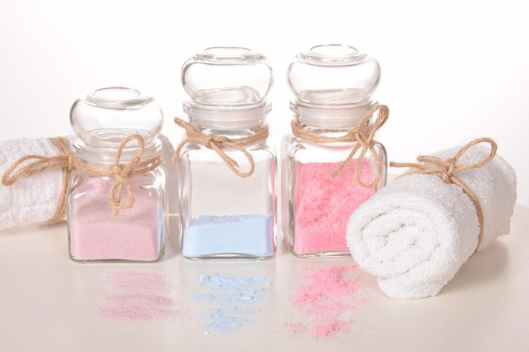 Jars of colorful bath salts with a rolled white towel.