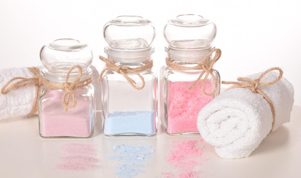 Jars of colorful bath salts with a rolled white towel.