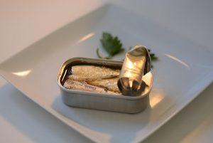 Tin of sardines on a white plate with parsley garnish.