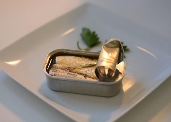 Tin of sardines on a white plate with parsley garnish.