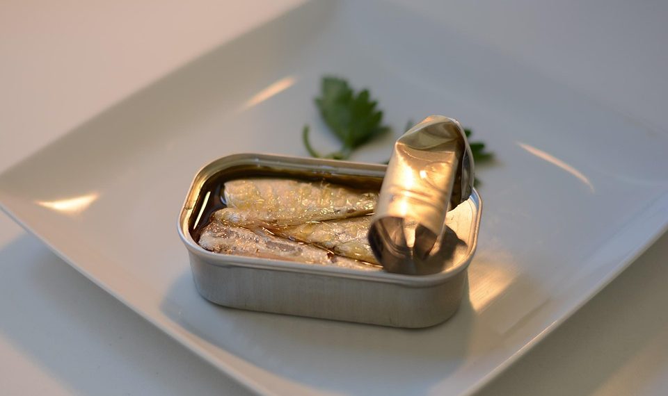 Tin of sardines on a white plate with parsley garnish.