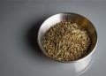 Bowl filled with cumin seeds on a gray surface.