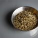 Bowl filled with cumin seeds on a gray surface.