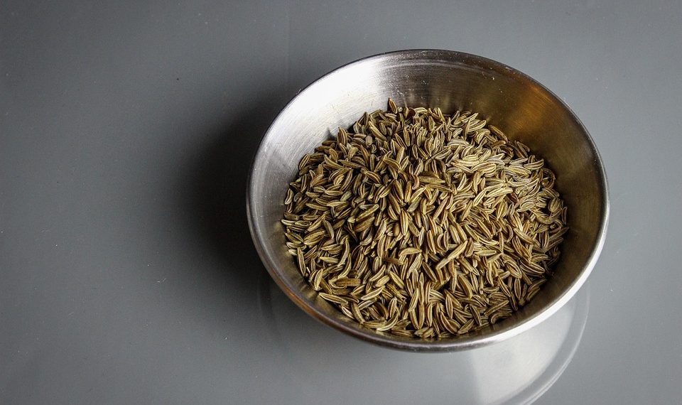 Bowl filled with cumin seeds on a gray surface.