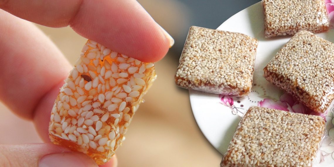 Sesame candy square held by fingers next to plate of sweets.