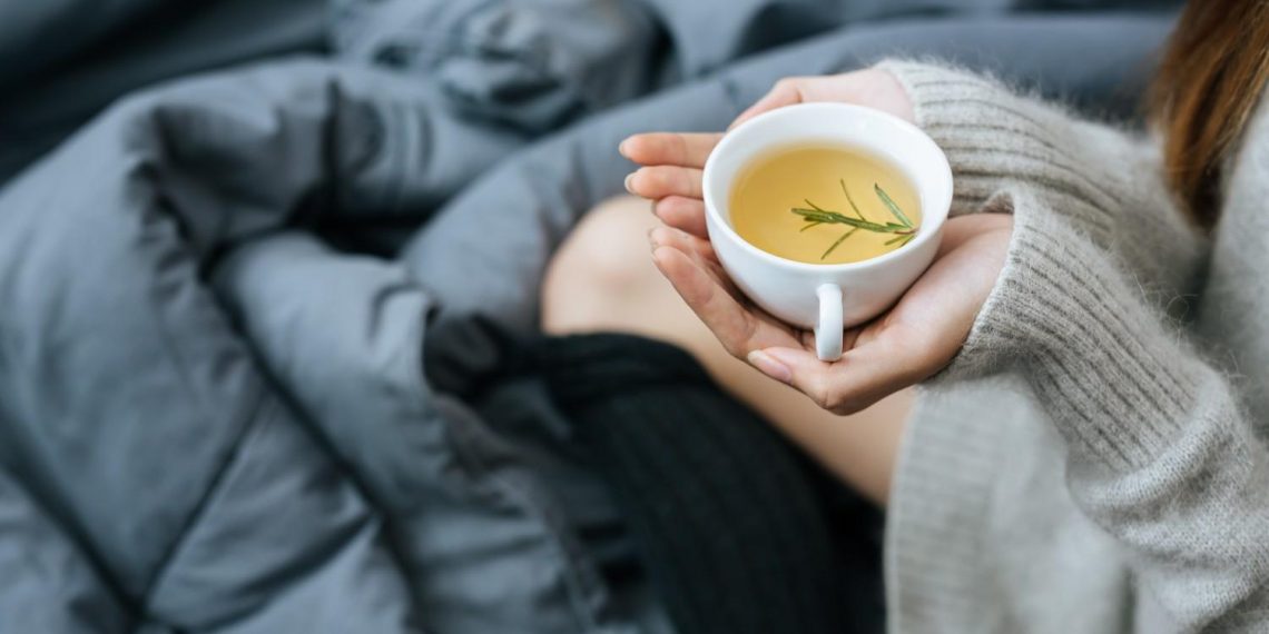Hands holding herbal tea mug on cozy blanket.