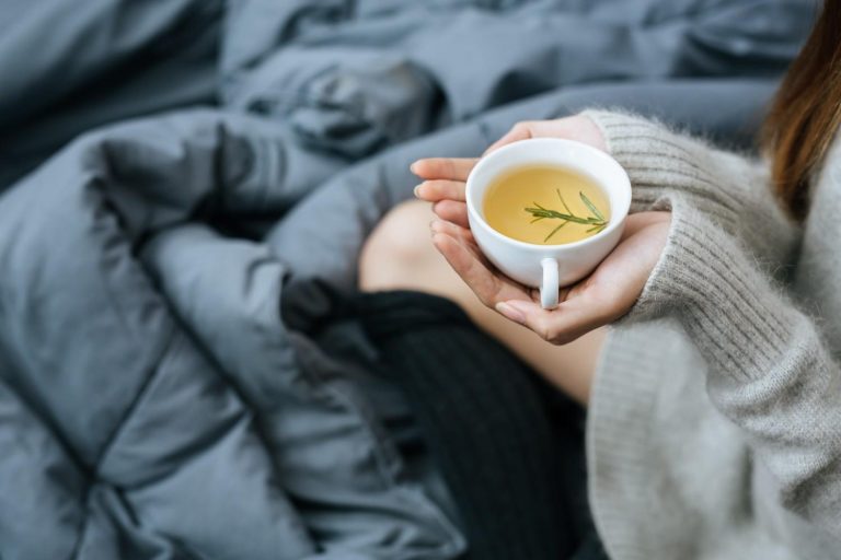 Hands holding herbal tea mug on cozy blanket.