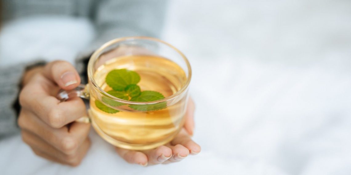 Warm herbal tea with mint in a clear cup held in cozy hands.