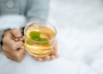 Warm herbal tea with mint in a clear cup held in cozy hands.