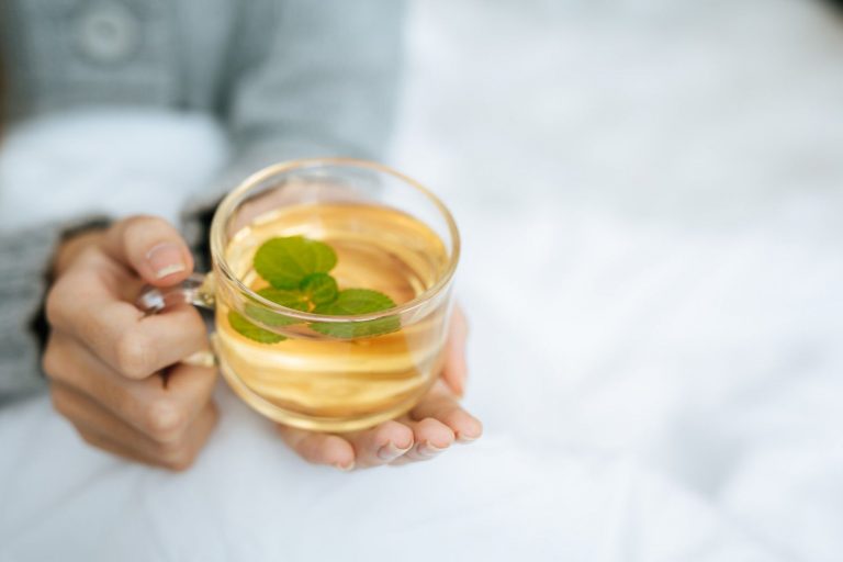 Warm herbal tea with mint in a clear cup held in cozy hands.