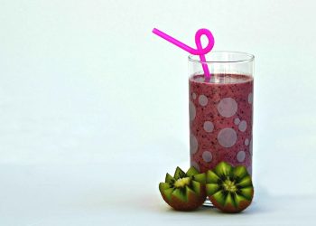 Kiwi smoothie with pink straw in a glass next to sliced kiwis.