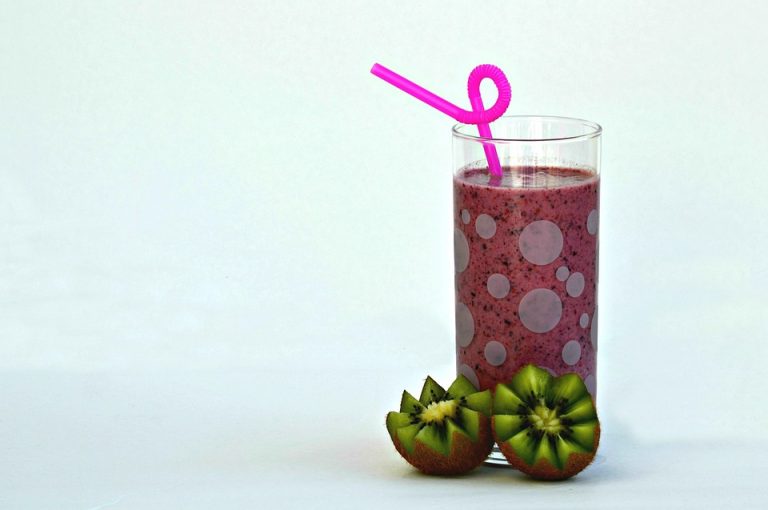 Kiwi smoothie with pink straw in a glass next to sliced kiwis.