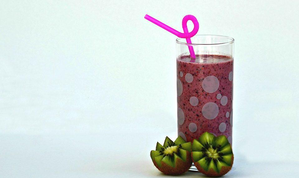 Kiwi smoothie with pink straw in a glass next to sliced kiwis.