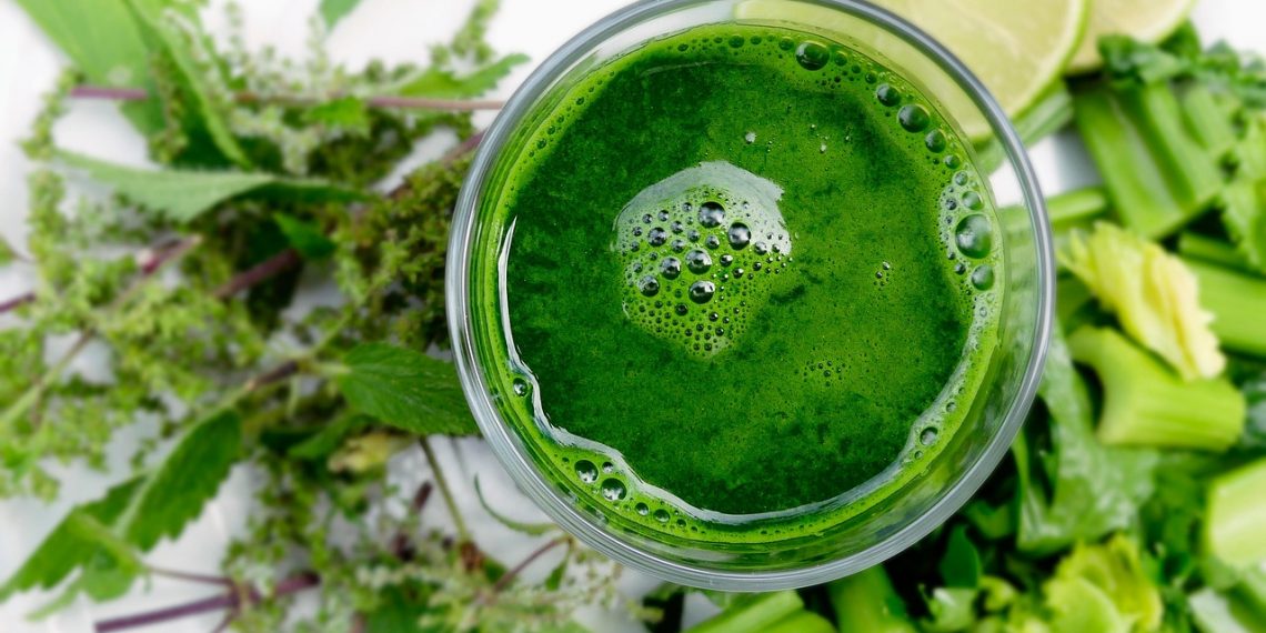 Green smoothie surrounded by fresh leafy greens and lime slices {focus_keyword}.