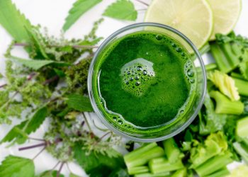 Green smoothie surrounded by fresh leafy greens and lime slices {focus_keyword}.