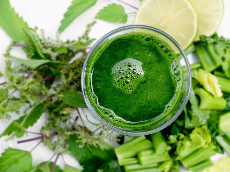 Green smoothie surrounded by fresh leafy greens and lime slices {focus_keyword}.