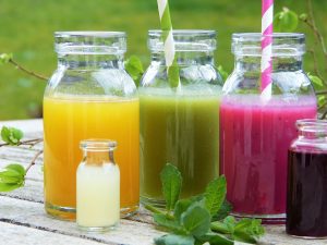 Colorful fruit juices in glass bottles with striped straws on a wooden table.