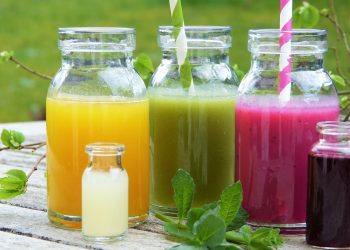 Colorful fruit juices in glass bottles with striped straws on a wooden table.