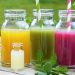 Colorful fruit juices in glass bottles with striped straws on a wooden table.